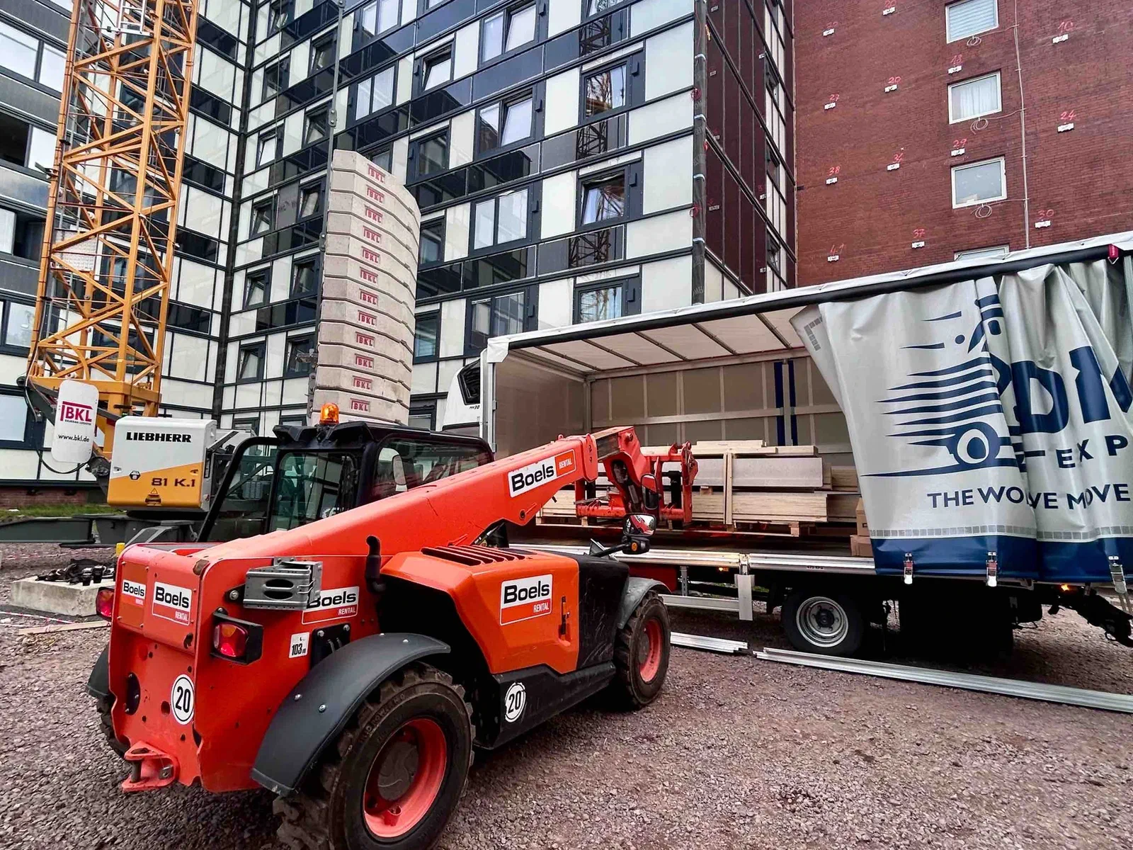 Ein Teleskoplader lädt eine Palette durch die geöffnete Seite eines Planenfahrzeugs von DMF Express auf einer Baustelle